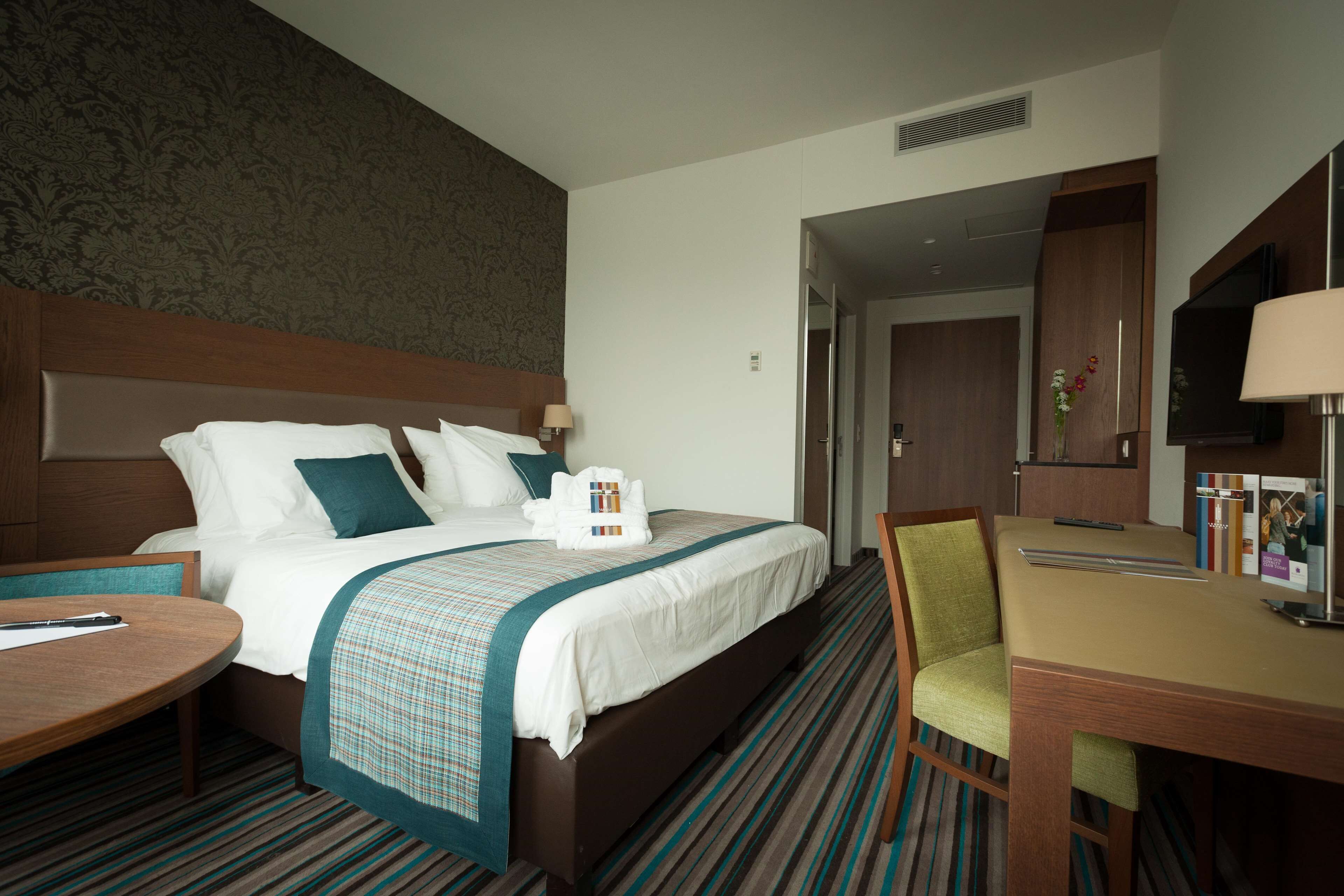 A hotel room with a large bed, a desk, a chair, and a television.
