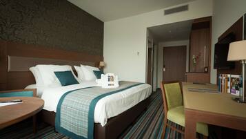 A hotel room with a large bed, a desk, a chair, and a television.