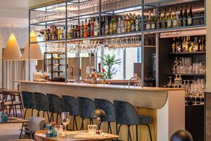Zona de bar con múltiples estantes llenos de botellas y vasos, una barra con una fuente decorativa, y un área de asientos con sillas y mesas.
