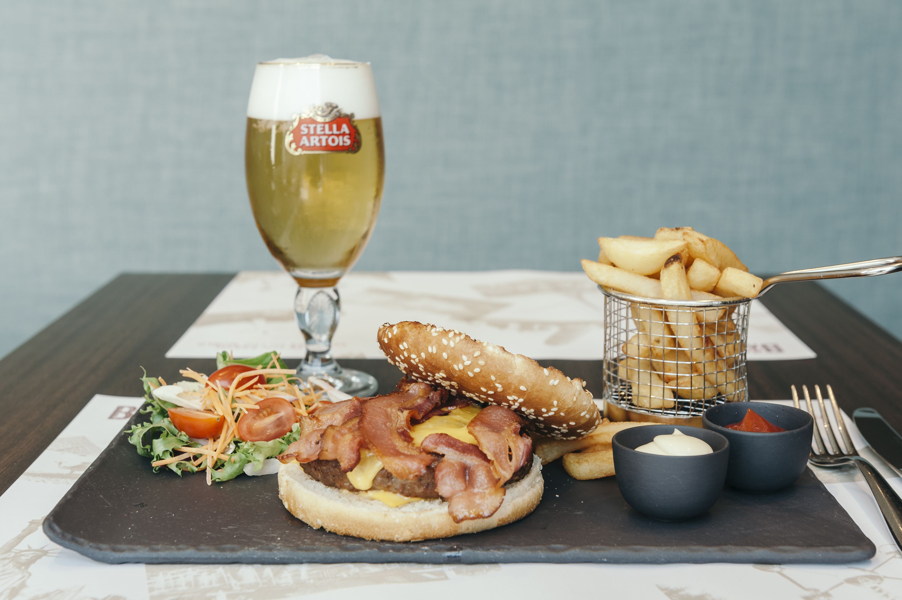 A meal with a burger, fries, salad, and a beer glass on a slate board.