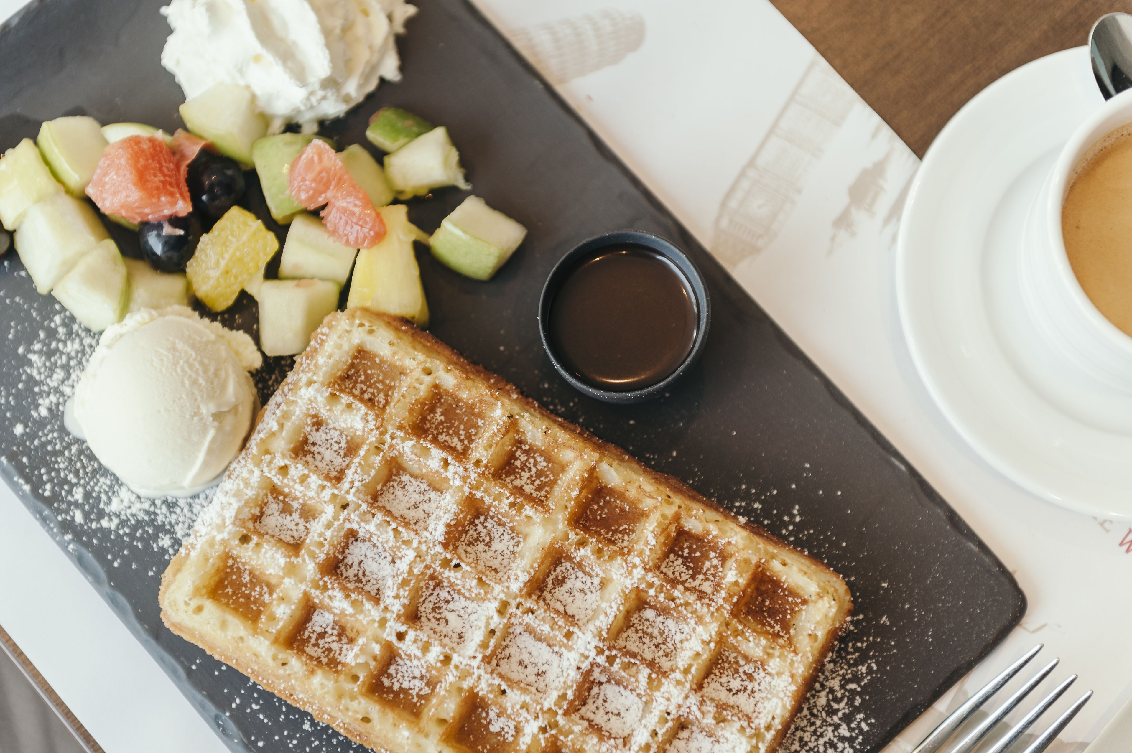 Une assiette de petit-déjeuner avec des gaufres, des fruits, de la glace et du sirop.