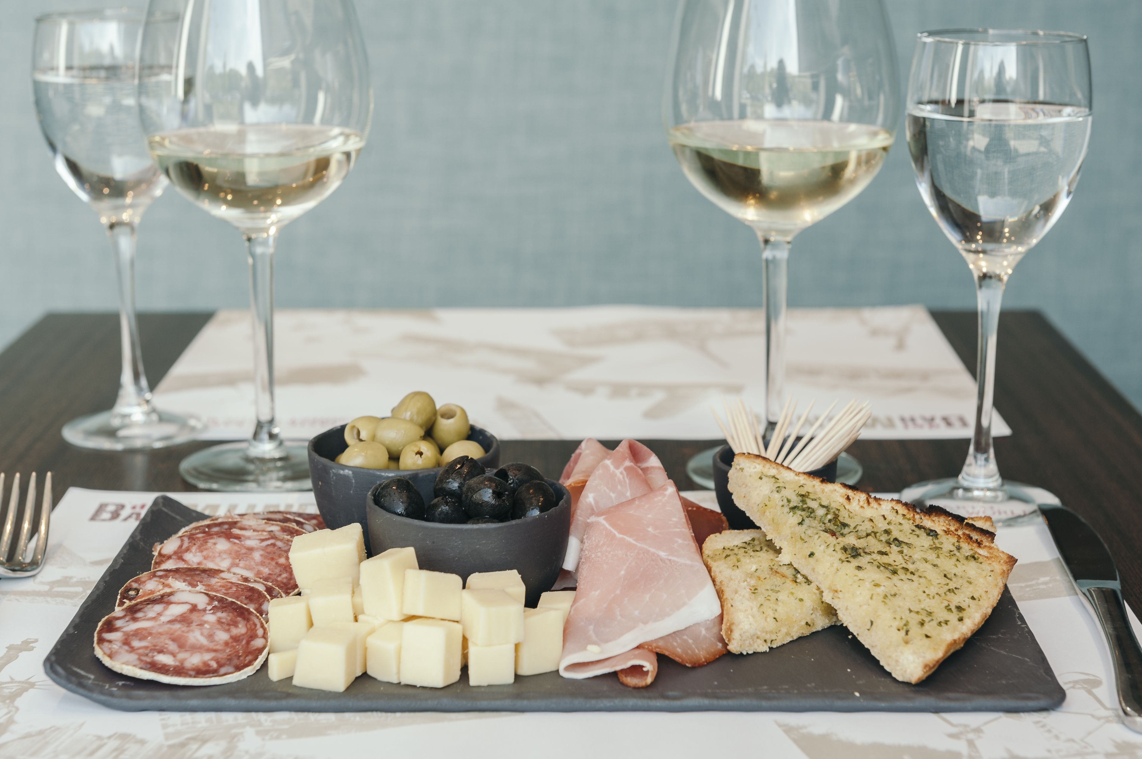 A charcuterie board with various meats, cheeses, olives, and bread, accompanied by wine glasses.