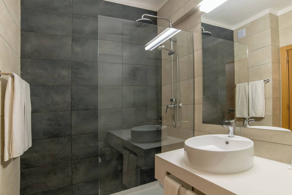 A modern bathroom with a glass-enclosed shower, a round sink, and a large mirror.