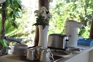 A table with a white vase of flowers, a toaster, and stacked plates. - AmaresA Resort & Skybar (Ko Pha-ngan)