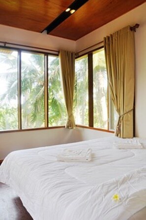 A bedroom with a large bed, beige curtains, and a view of palm trees through the window.
