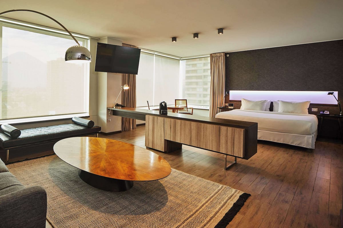 Une chambre d’hôtel moderne dotée d’un grand lit, d’un bureau avec une chaise, d’un canapé, d’une table basse et d’un téléviseur fixé au mur.