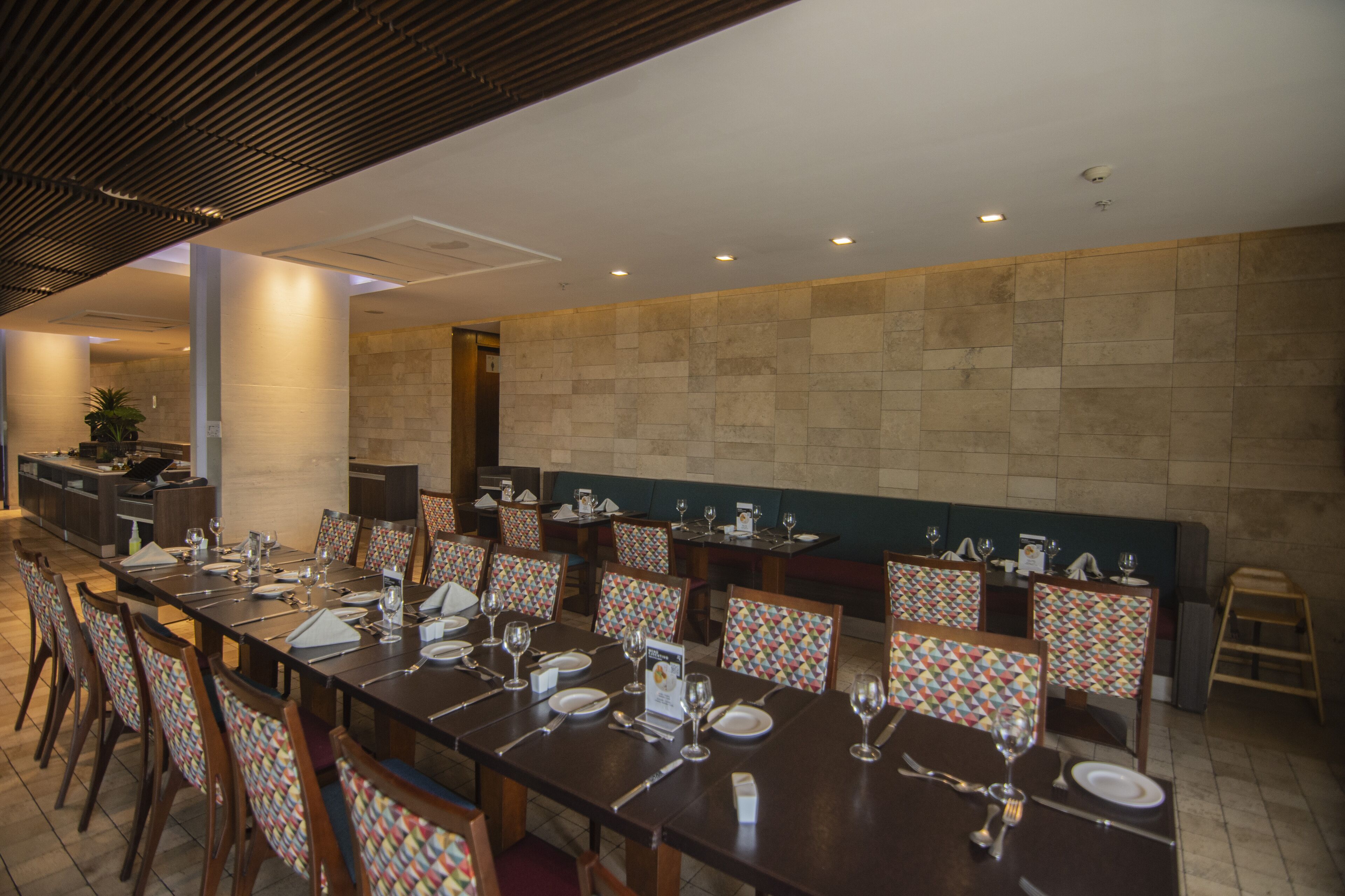 A dining area with multiple tables set for service, chairs with patterned upholstery, and a stone-tiled wall.