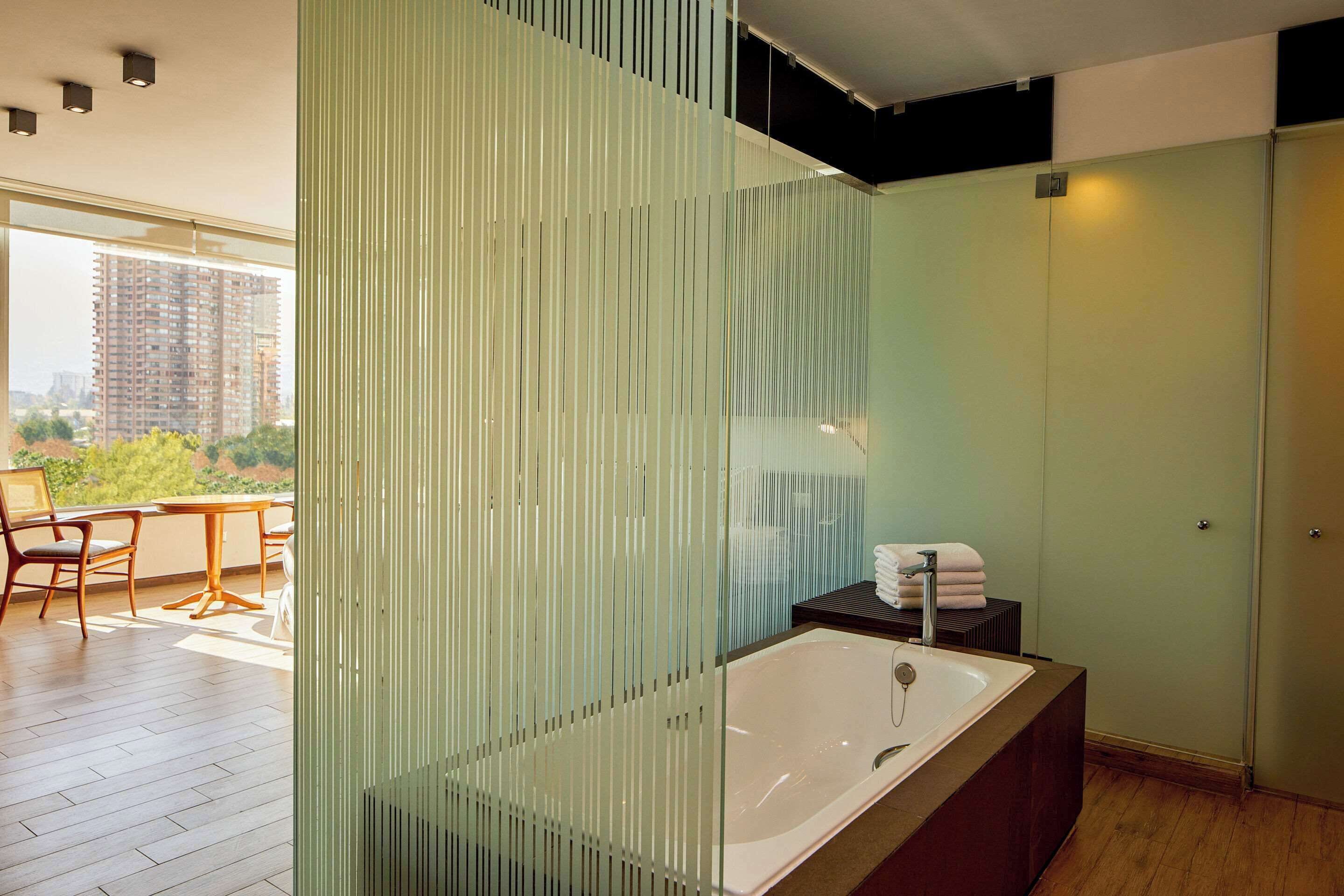 Un baño moderno con una bañera grande, un separador de vidrio y vistas a un paisaje urbano.