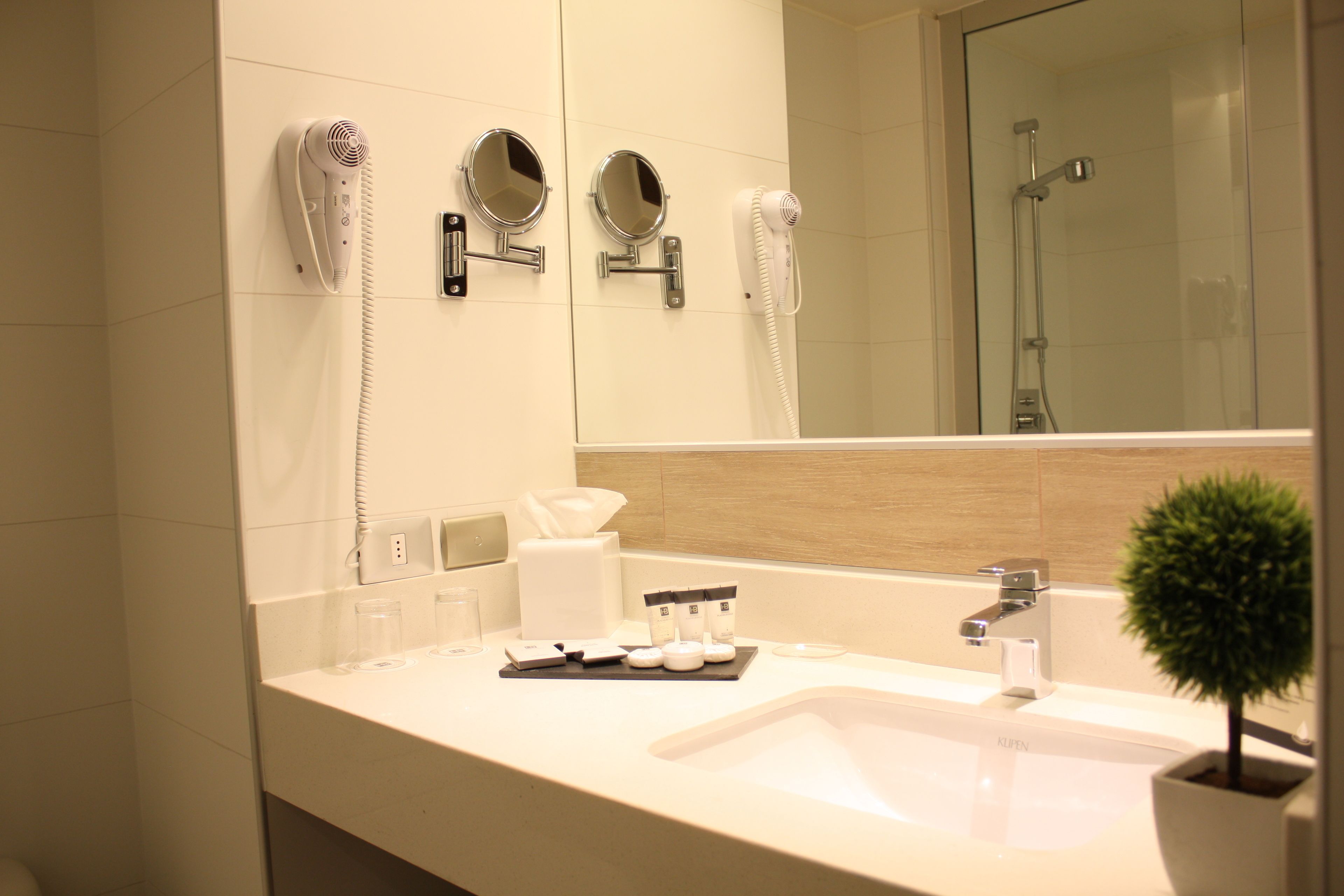 Un bagno moderno con uno specchio grande, un asciugacapelli, un lavandino e una piccola pianta in vaso.