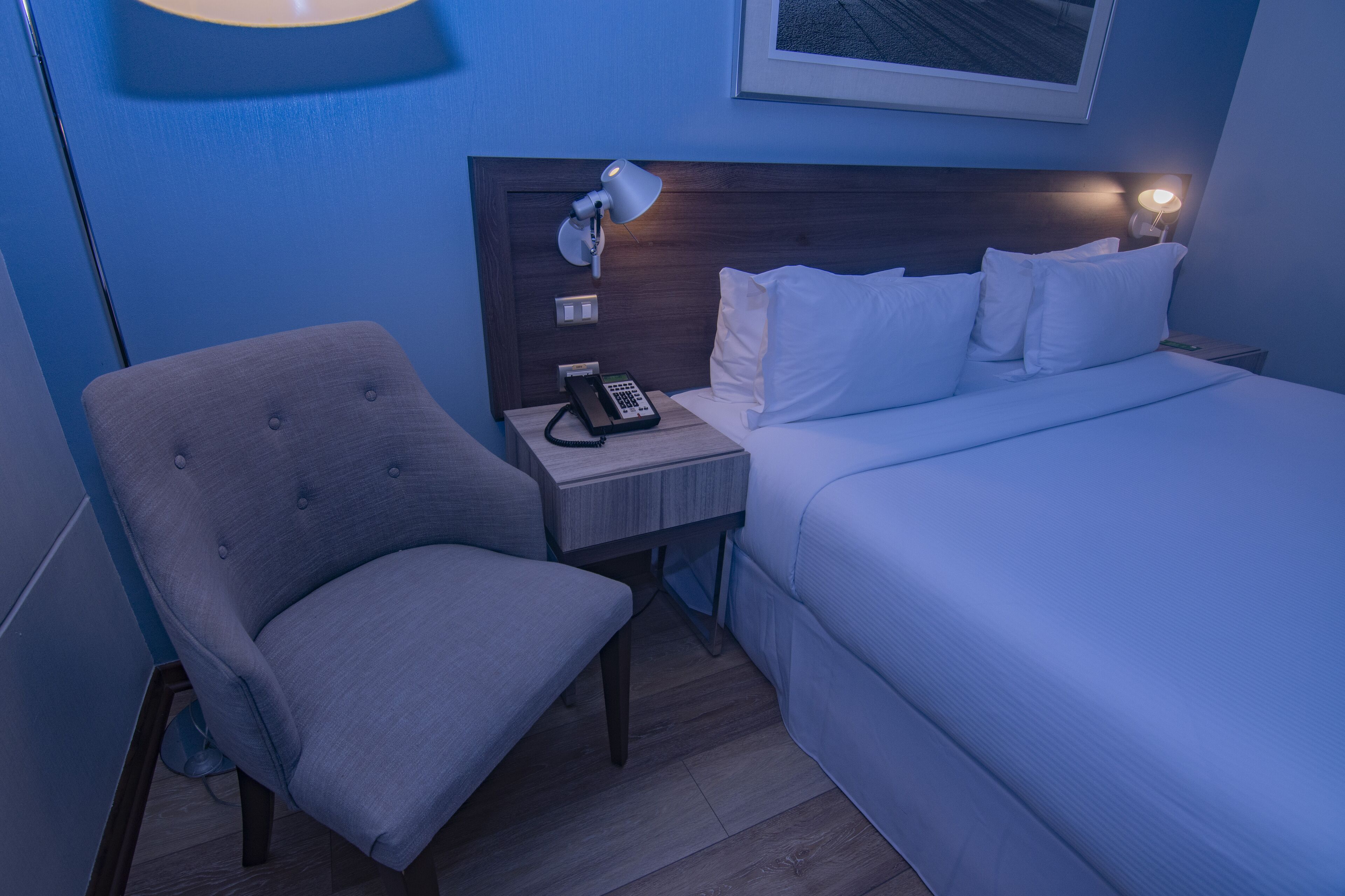 Une chambre d’hôtel avec un lit, une chaise, une table de chevet avec une lampe et un téléphone.