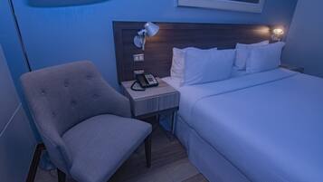 Une chambre d’hôtel avec un lit, une chaise, une table de chevet avec une lampe et un téléphone.