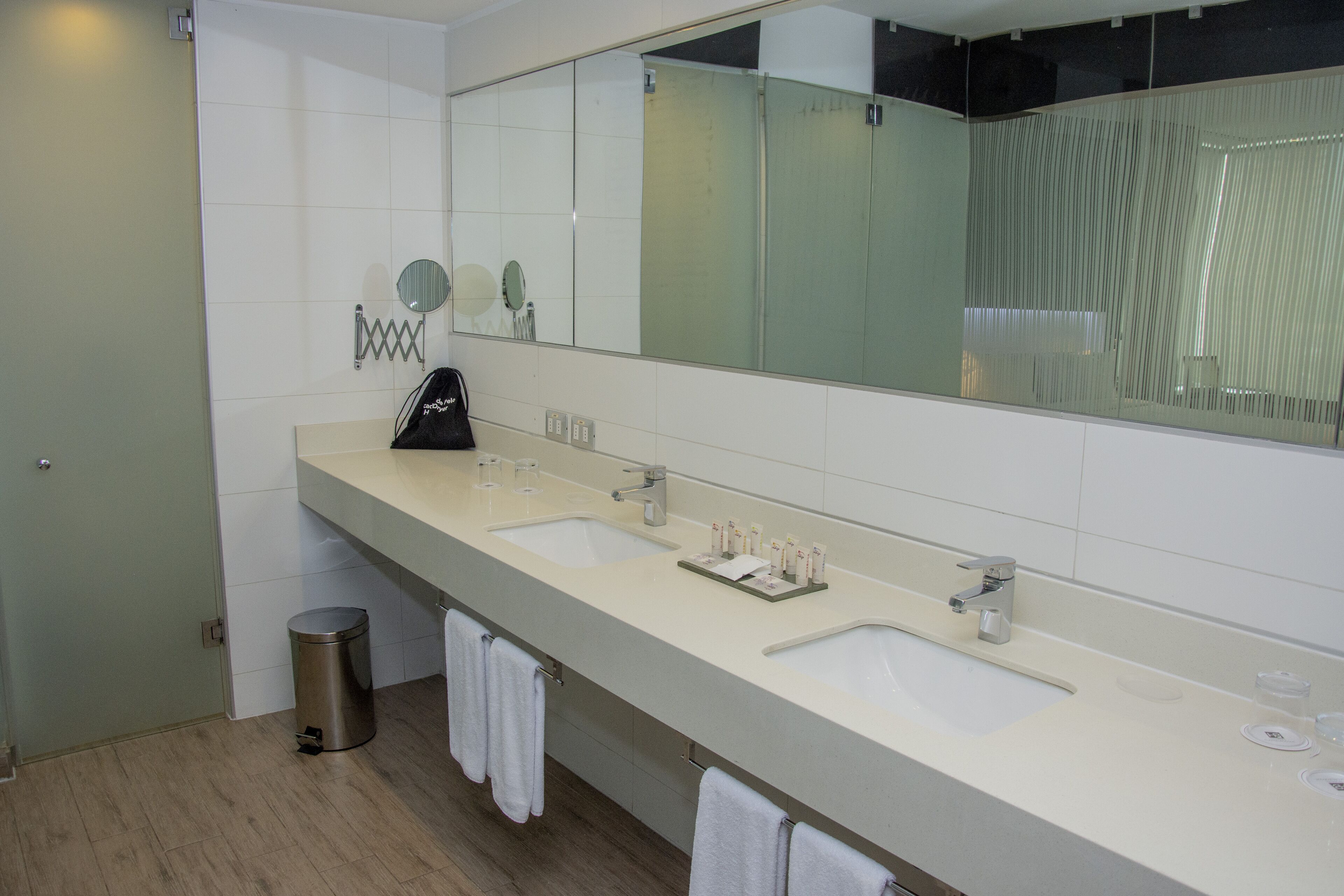 Un baño moderno con dos lavamanos, un espejo grande y un cesto de basura.