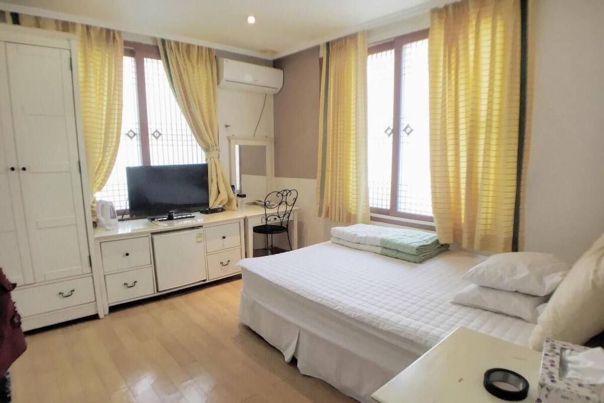 A bedroom with a bed, a desk, a chair, a TV, and a wardrobe.