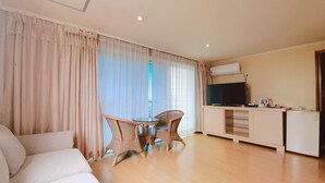 Una sala de estar con sofá, mesa de comedor con sillas, televisor y kitchenette.