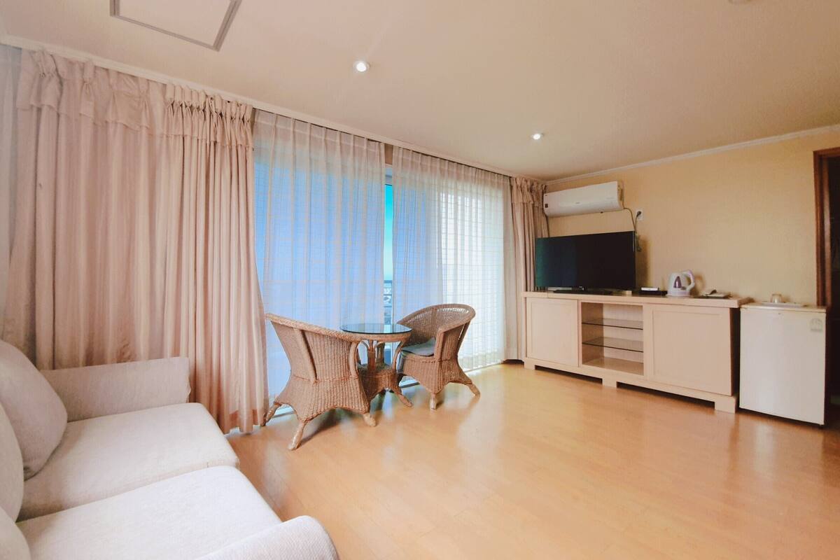 A living room with a sofa, a dining table with chairs, a television, and a kitchenette.