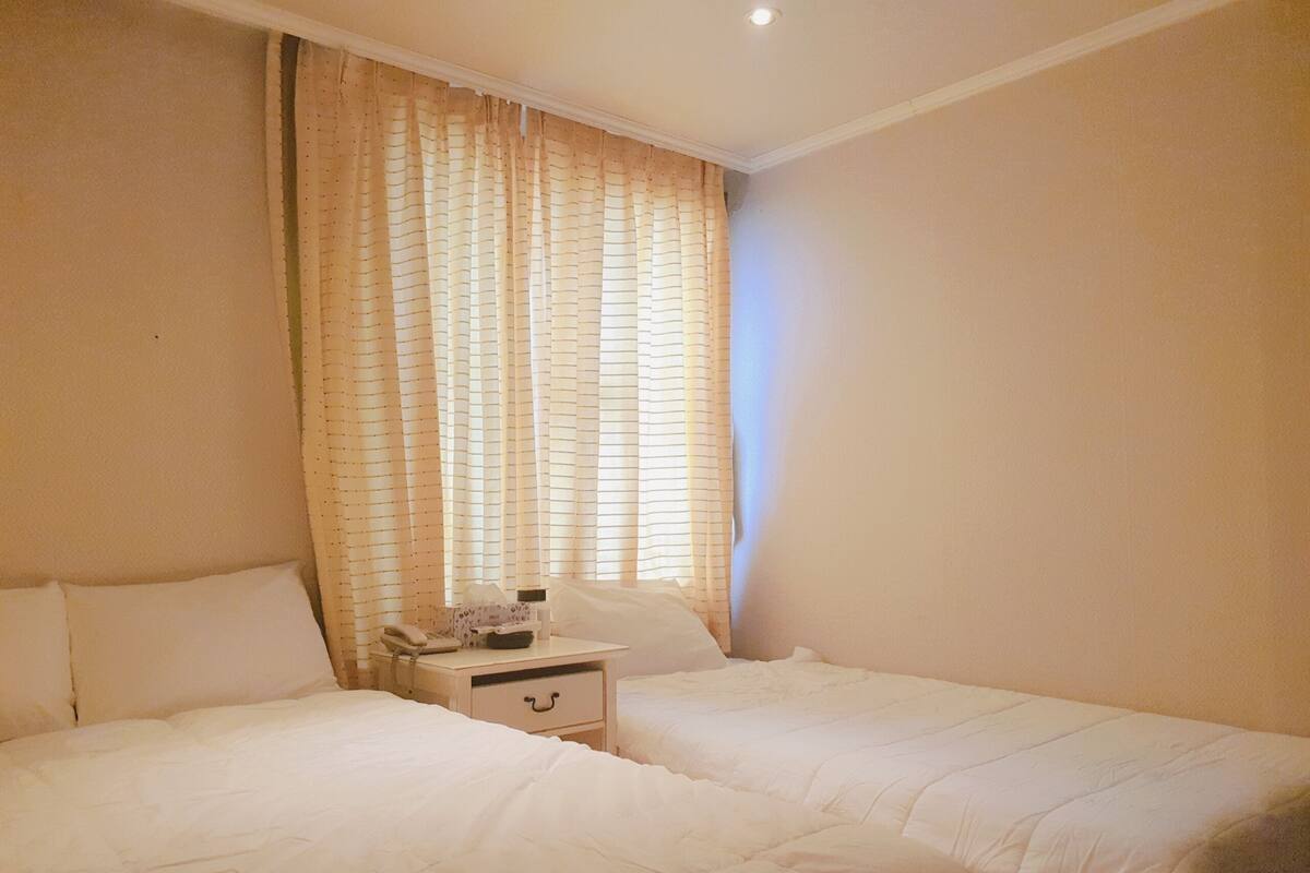 A bedroom with two beds, a nightstand, and a window with curtains.