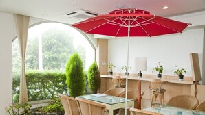 Un comedor con sillas de mimbre, una mesa de vidrio y un paraguas rojo.