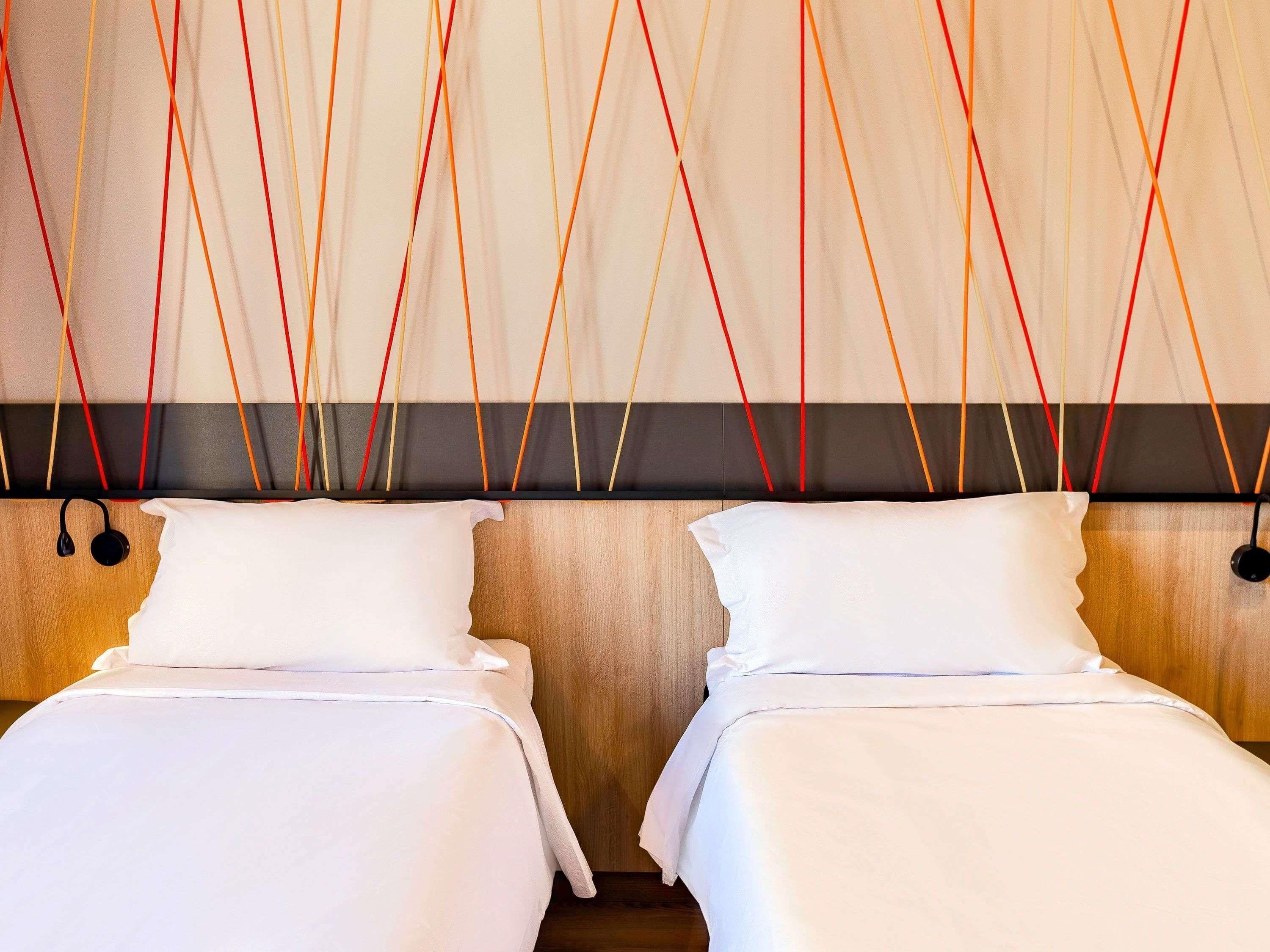 Habitación de hotel con dos camas, cabecera de madera y pared con diseño geométrico.