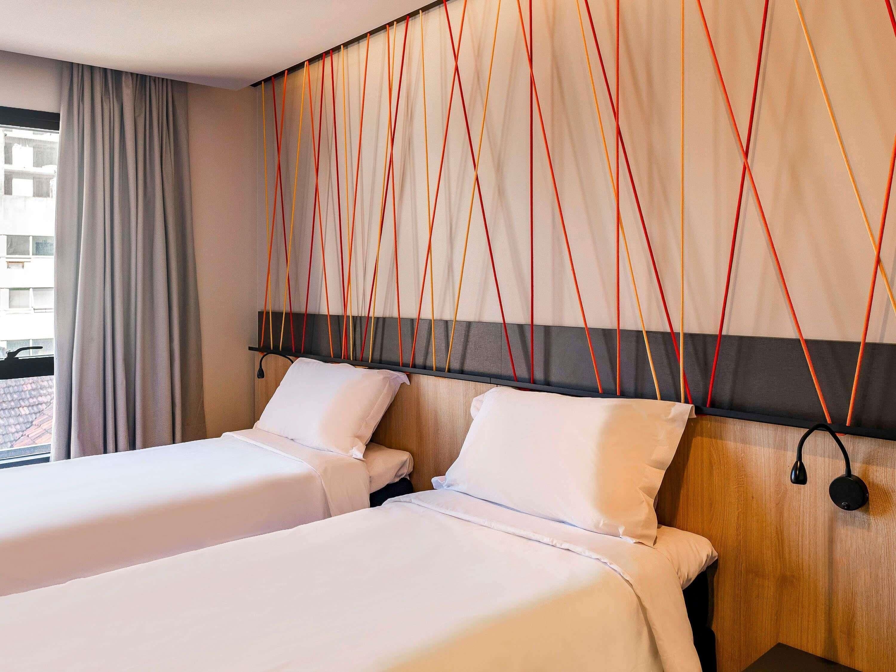 Habitación de hotel con dos camas, un cabecero de madera y una cortina.