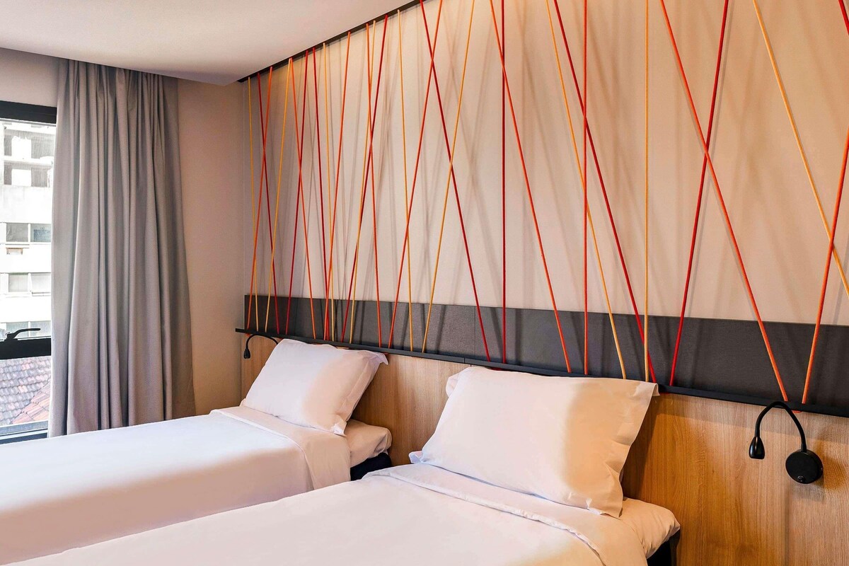 Een hotelkamer met twee bedden, een houten hoofdbord en een gordijn.