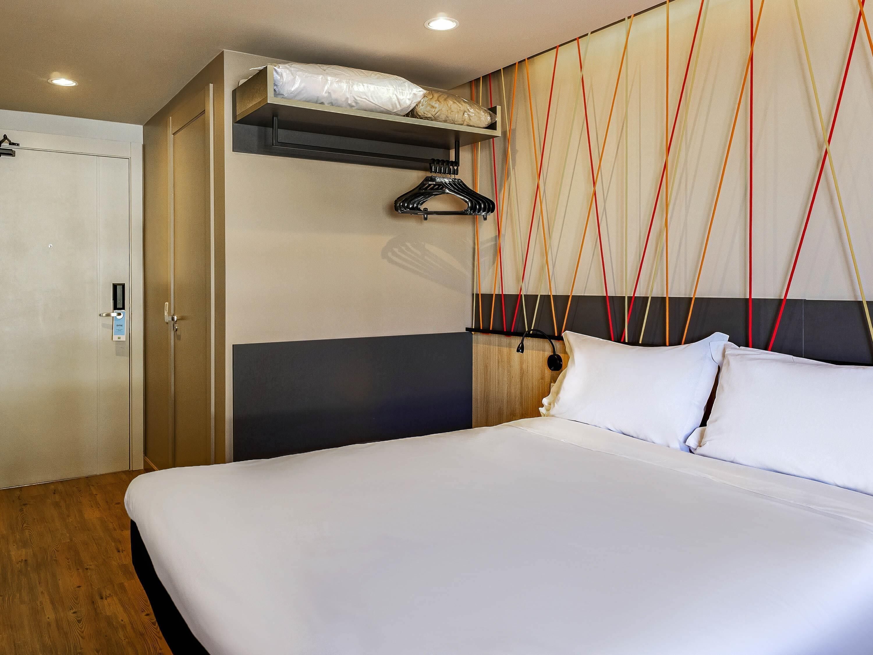Quarto de hotel com cama, guarda-roupa e parede com padrão geométrico.