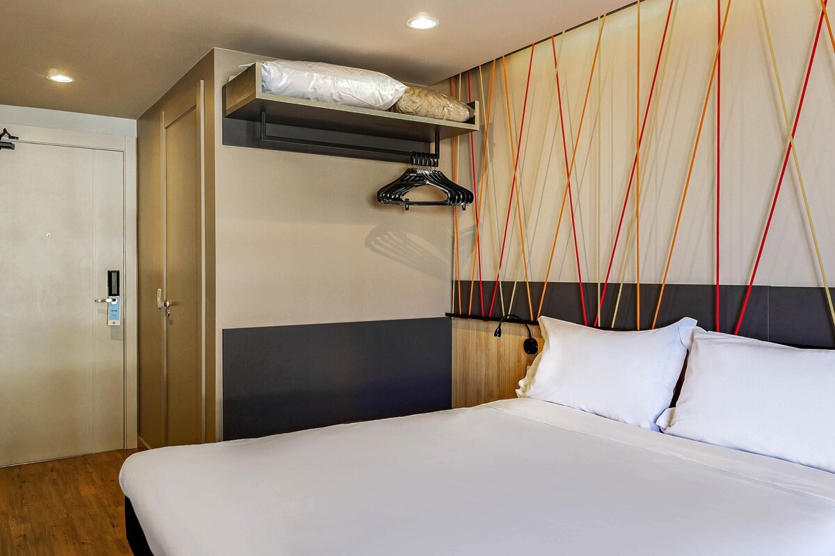 Een hotelkamer met een bed, een kledingkast en een muur met een geometrisch patroon.