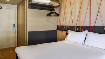 Quarto de hotel com cama, guarda-roupa e parede com padrão geométrico.