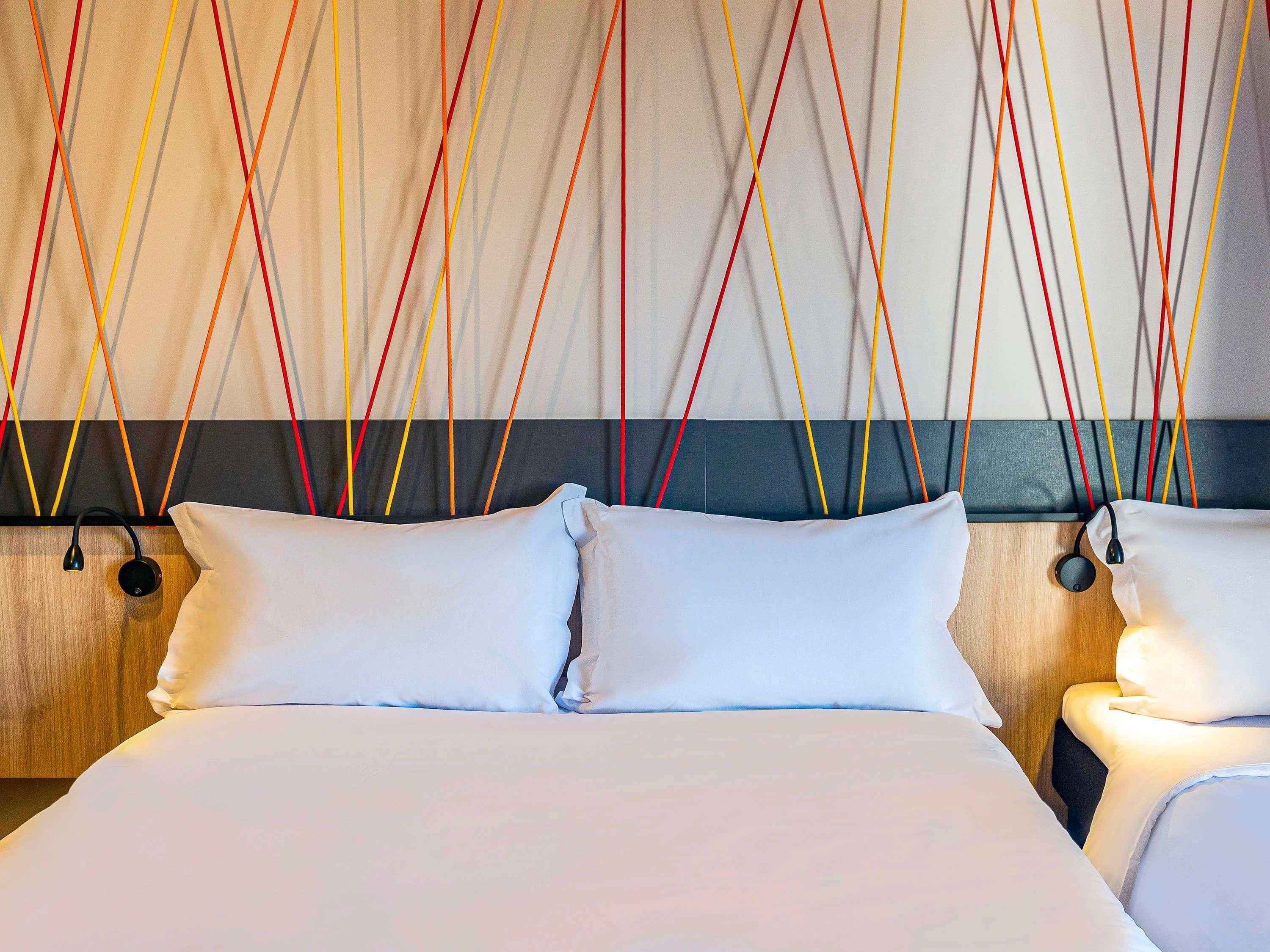 A hotel room with a large bed, two bedside tables, and a wall with colorful hanging cords.