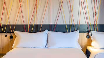 Een hotelkamer met een groot bed, twee nachtkastjes en een muur met kleurrijke hangende snoeren.