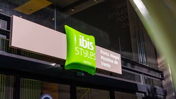A sign for 'ibis Styles Hotels' with a green logo and text indicating 'Porto Alegre' and 'Moninhos de Vento'.