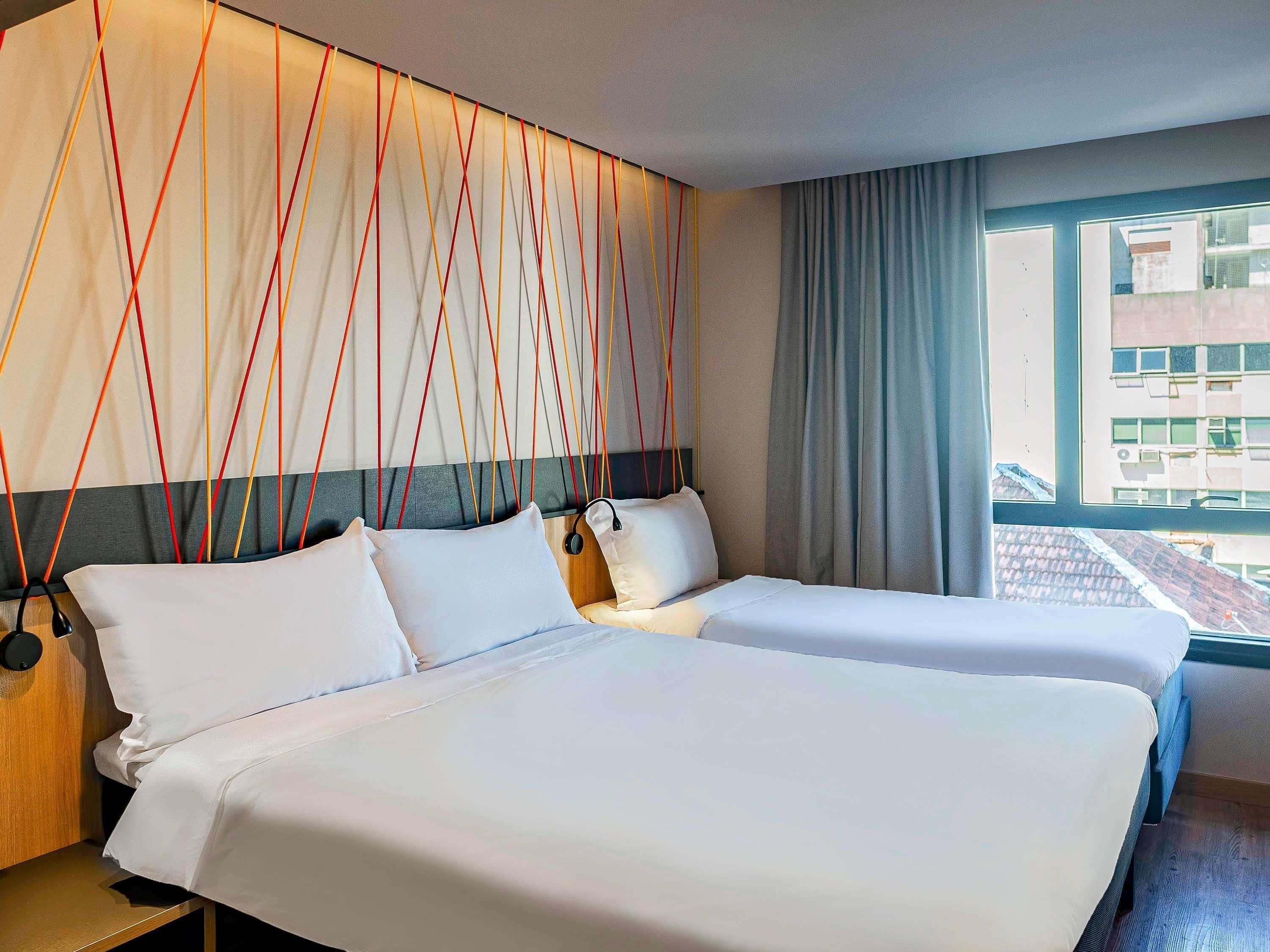 Quarto de hotel com duas camas, uma janela grande e vista para a cidade.