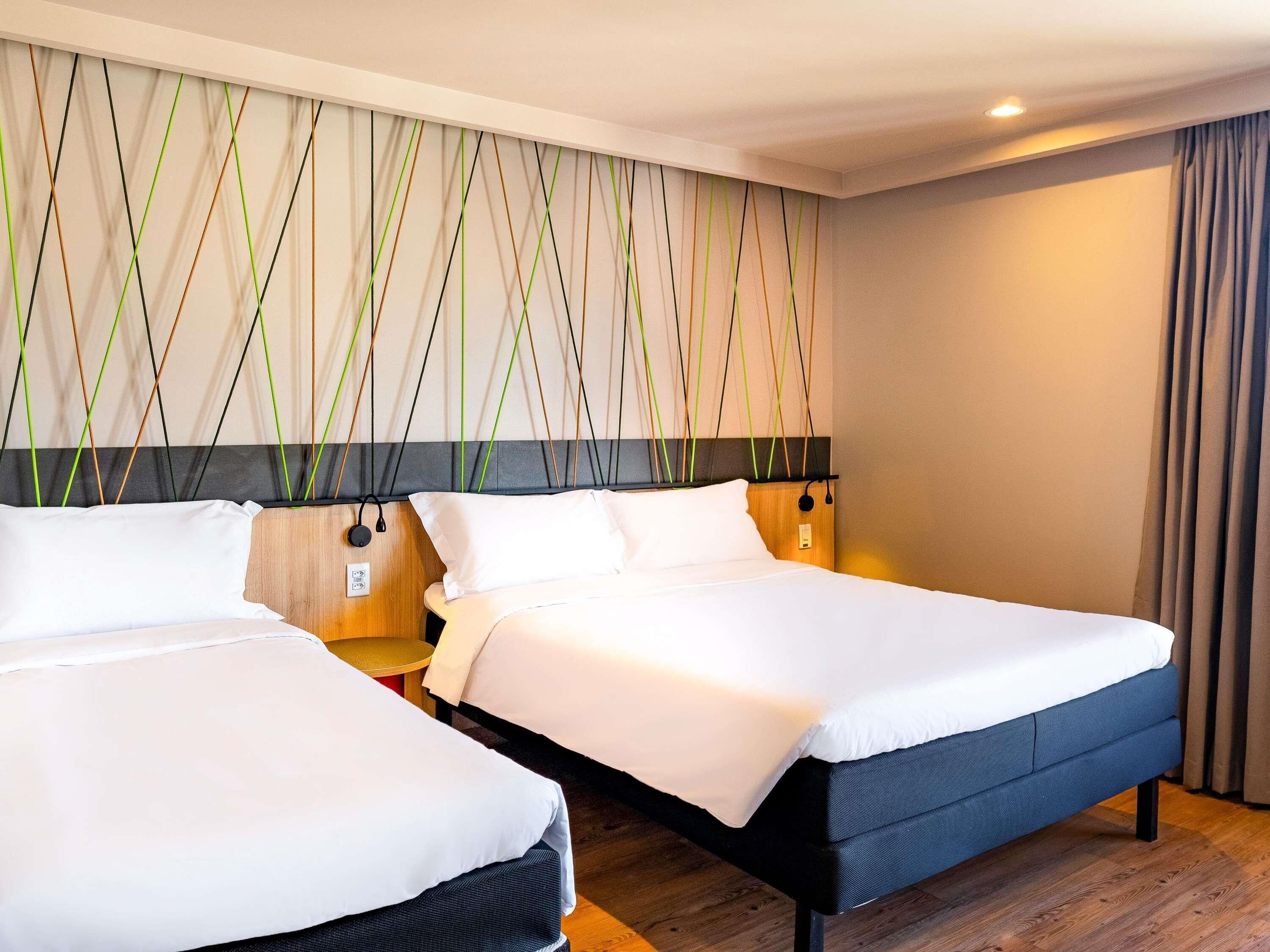 Quarto de hotel com duas camas, piso de madeira e parede com padrão geométrico.