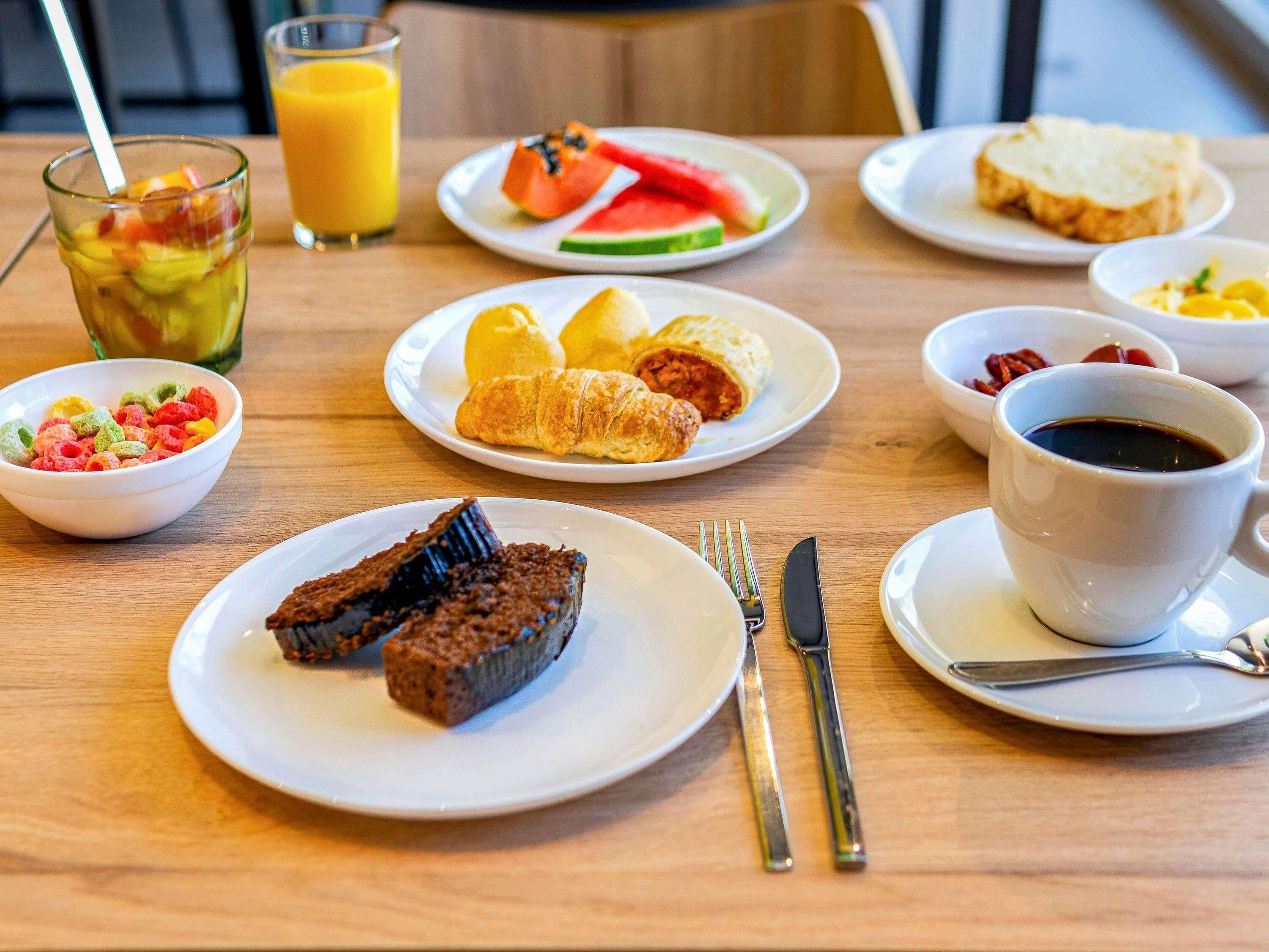Une table mise pour le petit-déjeuner, avec différents aliments disposés sur des assiettes, un verre de jus d’orange et une tasse de café.