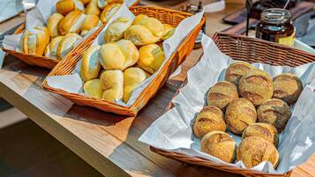 Uma mesa de buffet com diversos produtos de panificação, incluindo pães e doces, dispostos em cestos.