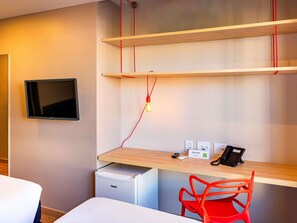 Een hotelkamer met een bed, een bureau met telefoon, een kleine koelkast en een aan de muur bevestigde televisie.