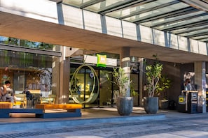 Een modern gebouw met glazen entree, terras en potplanten.