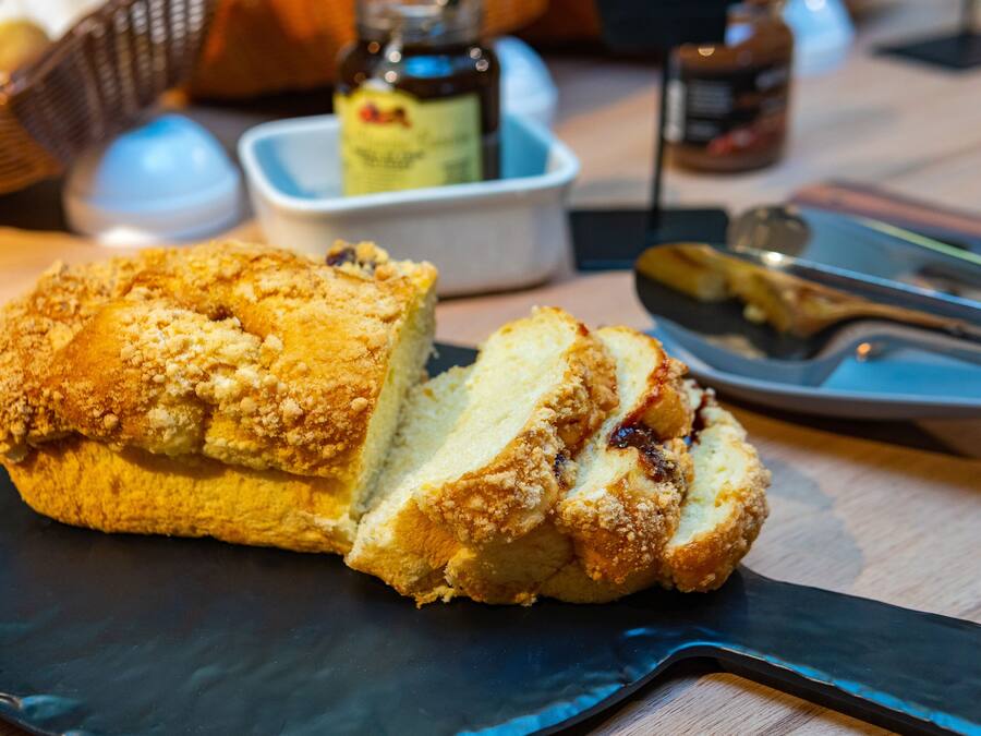 A loaf of bread on a dark plate with a knife and a small bowl in the background.