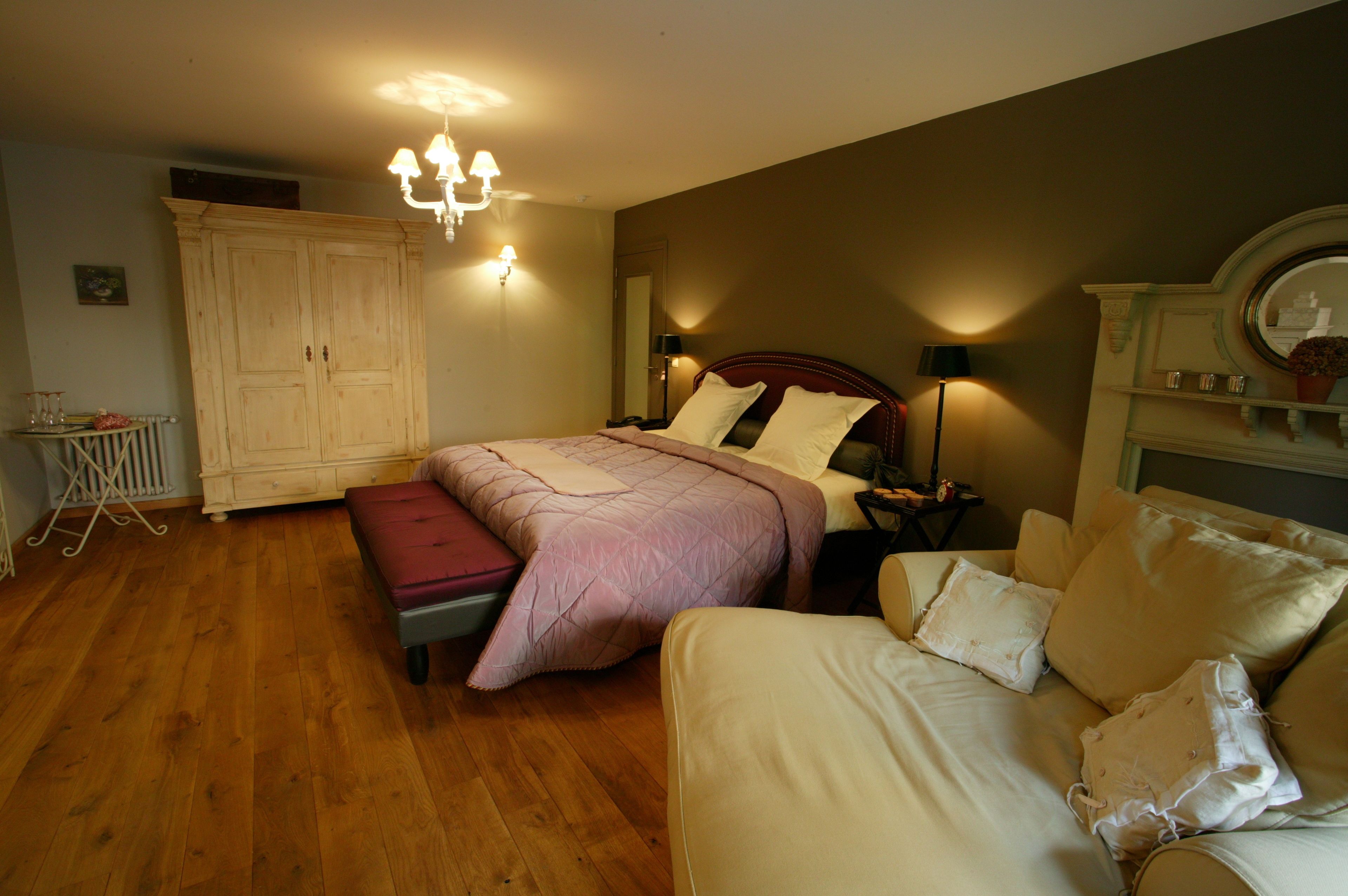 A bedroom with a large bed, a wooden floor, a wardrobe, and a bedside table with a lamp.