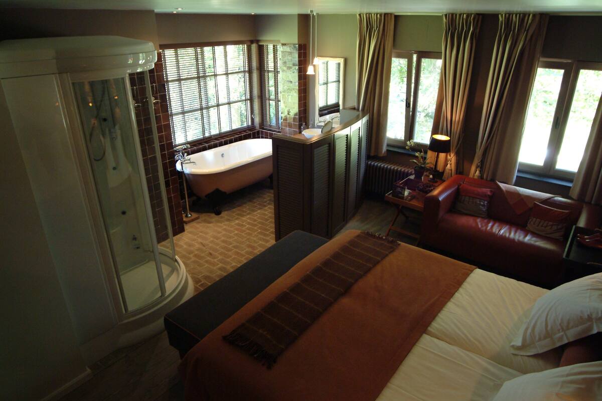 A hotel room with a bathtub, a bed, a desk, and a window with curtains.