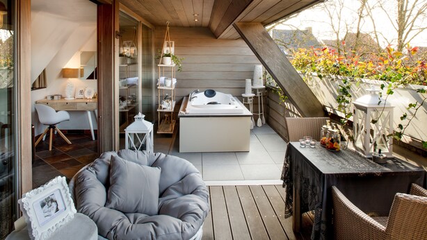 A modern, open-plan living space with a wooden ceiling, a cozy seating area, a dining table, and a large window overlooking a garden. - Charmehotel Manoir Ogygia (Poperinge)
