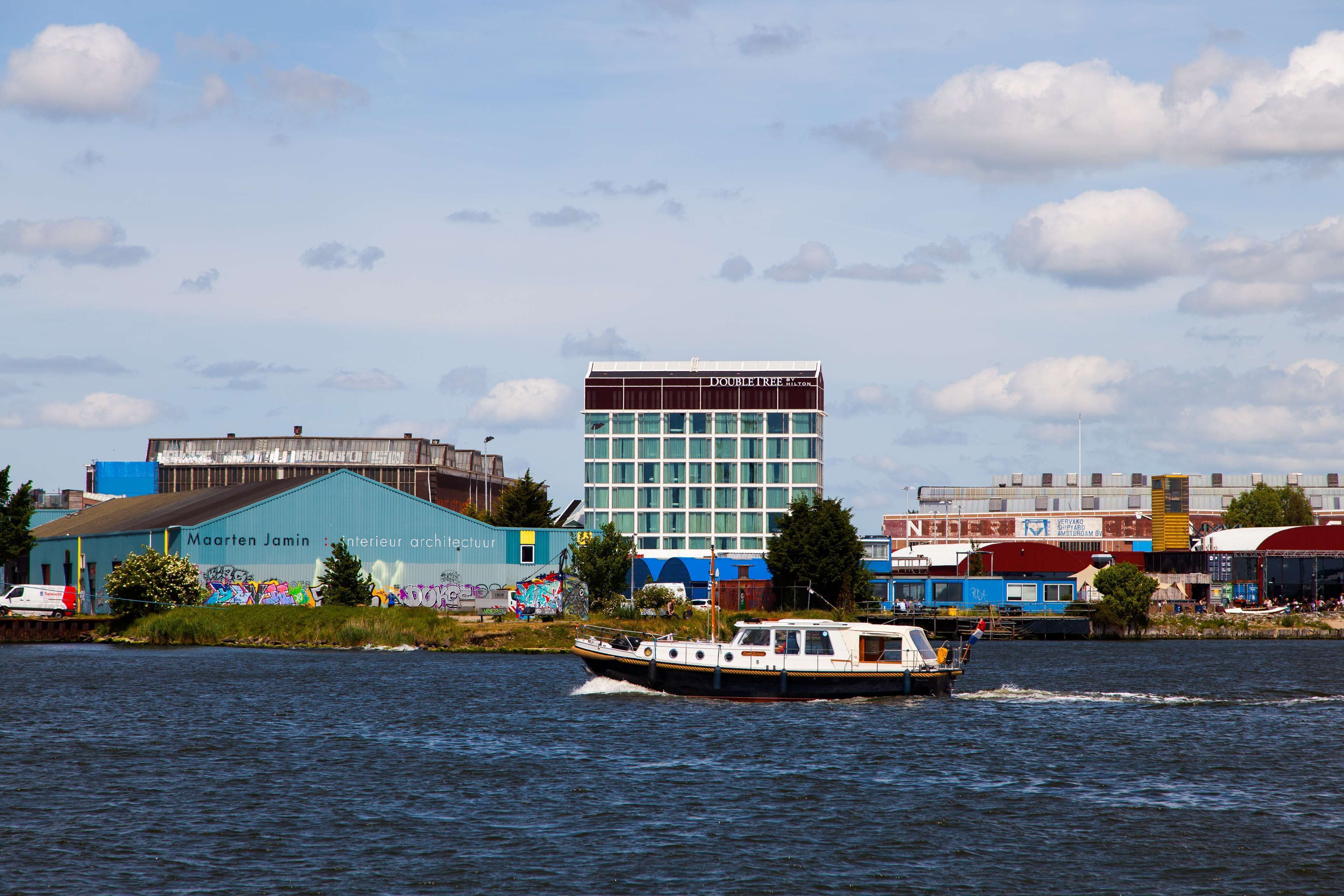A river with a boat in motion, buildings in the background, and a large building with 'DOUBLETREE' written on it.