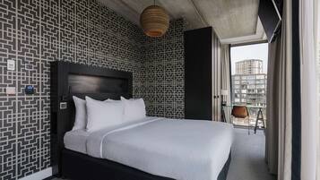 Une chambre d’hôtel moderne avec un grand lit, un papier peint à motifs, un luminaire suspendu et une vue sur la ville par la fenêtre.