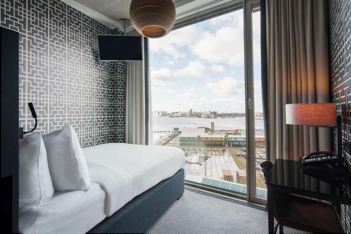 Une chambre d’hôtel avec un grand lit, un bureau, une chaise, une télévision et une vue sur la ville et l’eau.