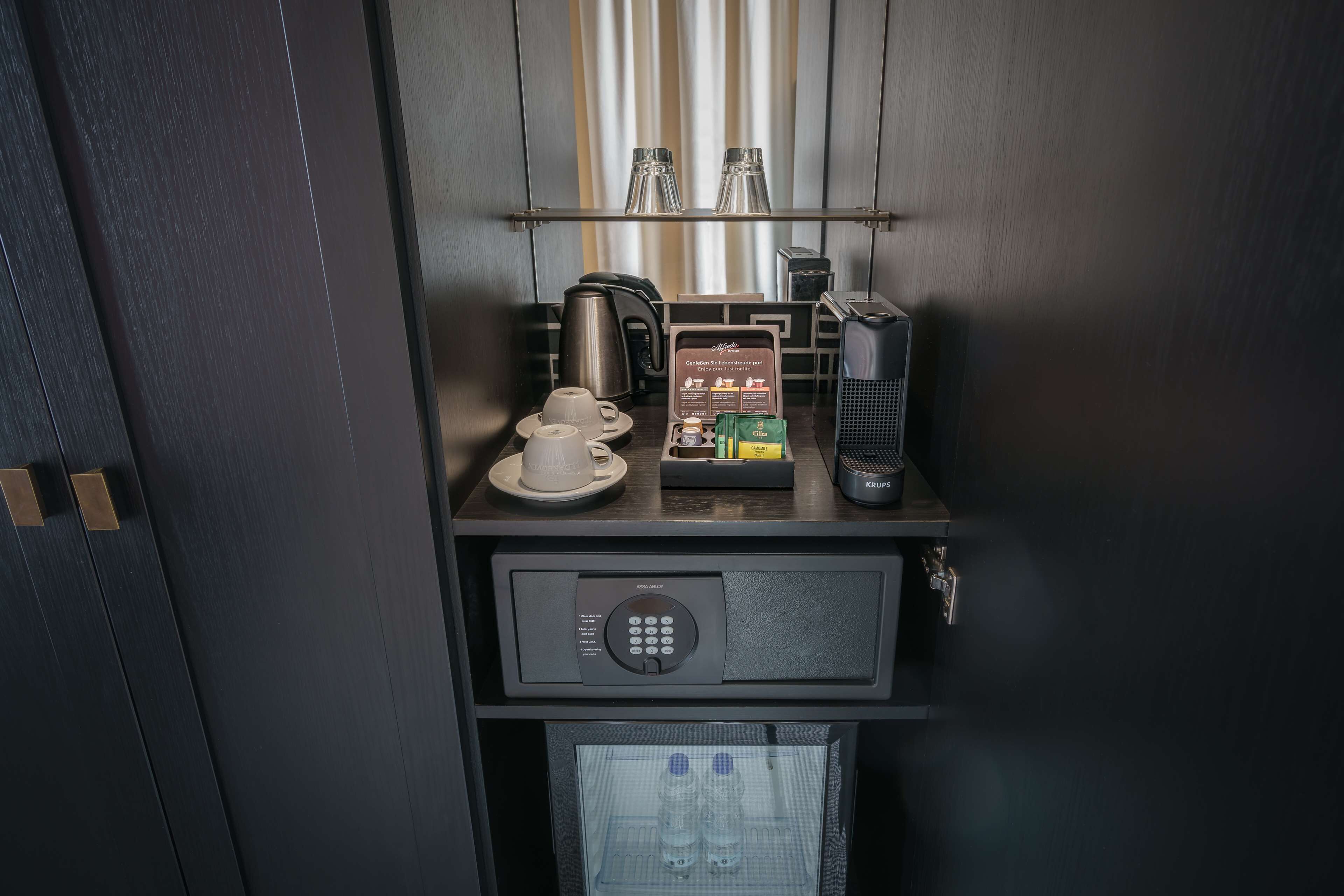A minibar with a coffee maker, tea set, and a Krups coffee grinder.