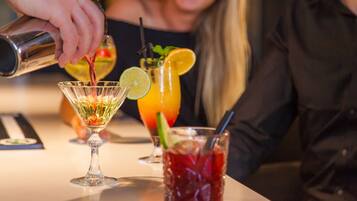 A bar setting with a person pouring a drink into a glass. There are three drinks on the counter, each with different garnishes.