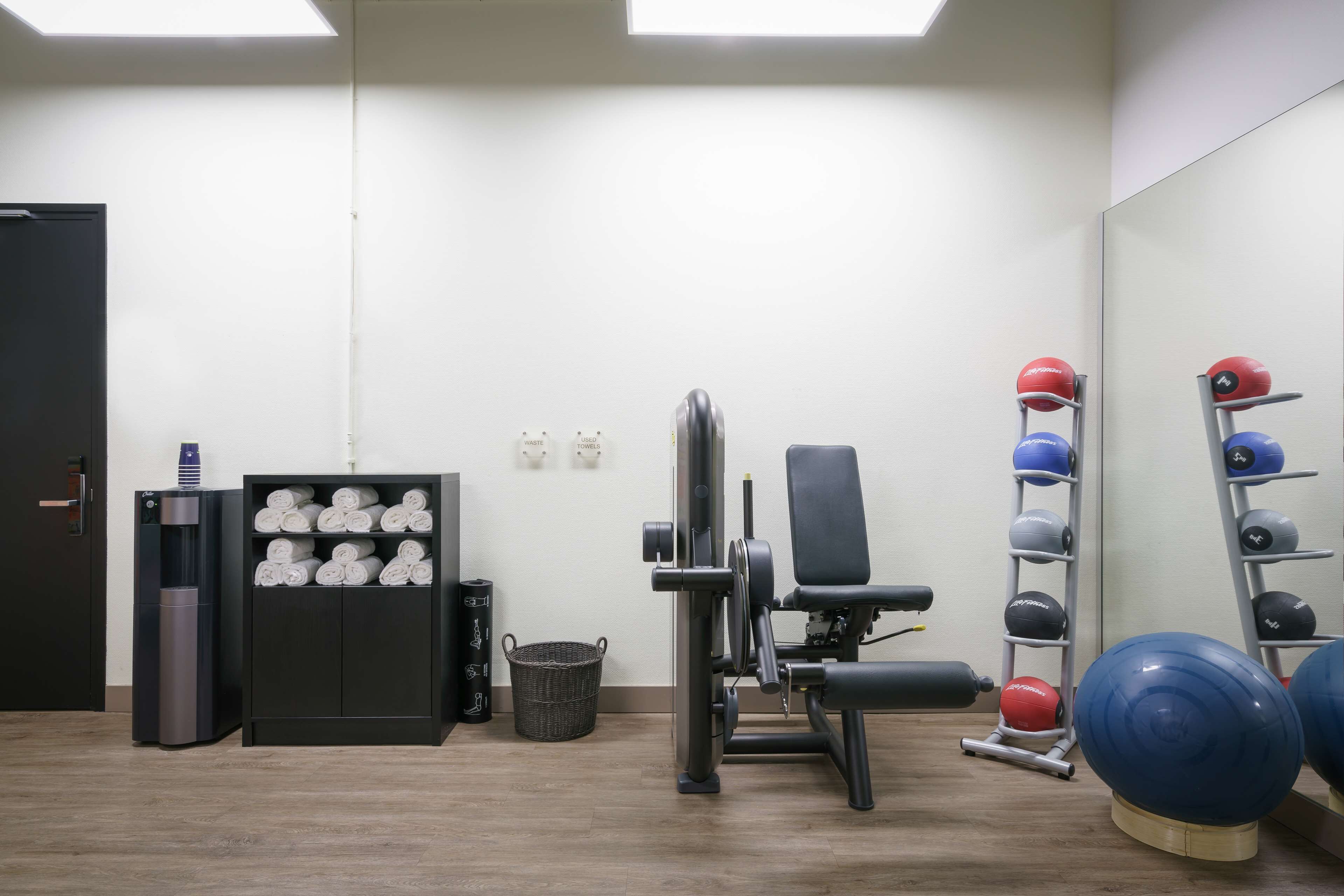 Ein Fitnessraum mit Trainingsgeräten, einem Wasserspender und ordentlich gestapelten Handtüchern.