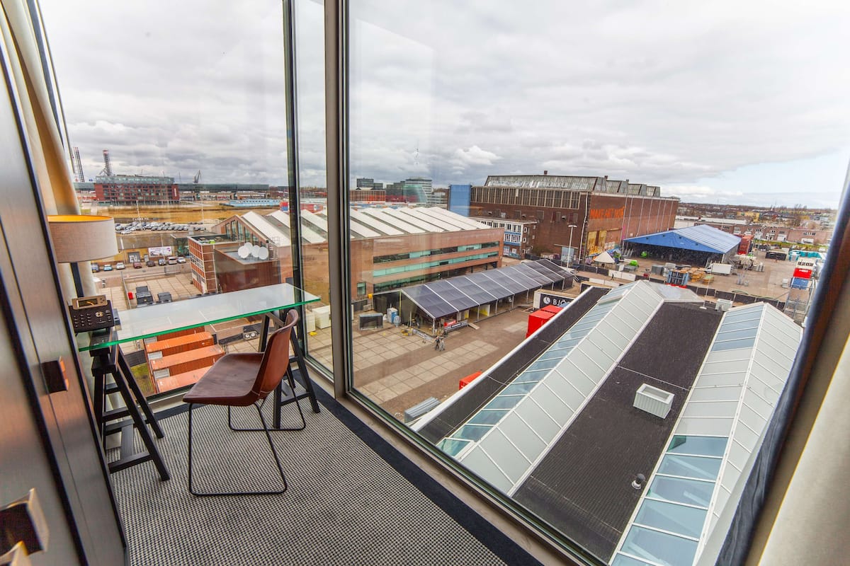 Une pièce dotée d’une grande fenêtre donnant sur une zone commerciale, notamment un bâtiment avec un toit bleu et des panneaux solaires.