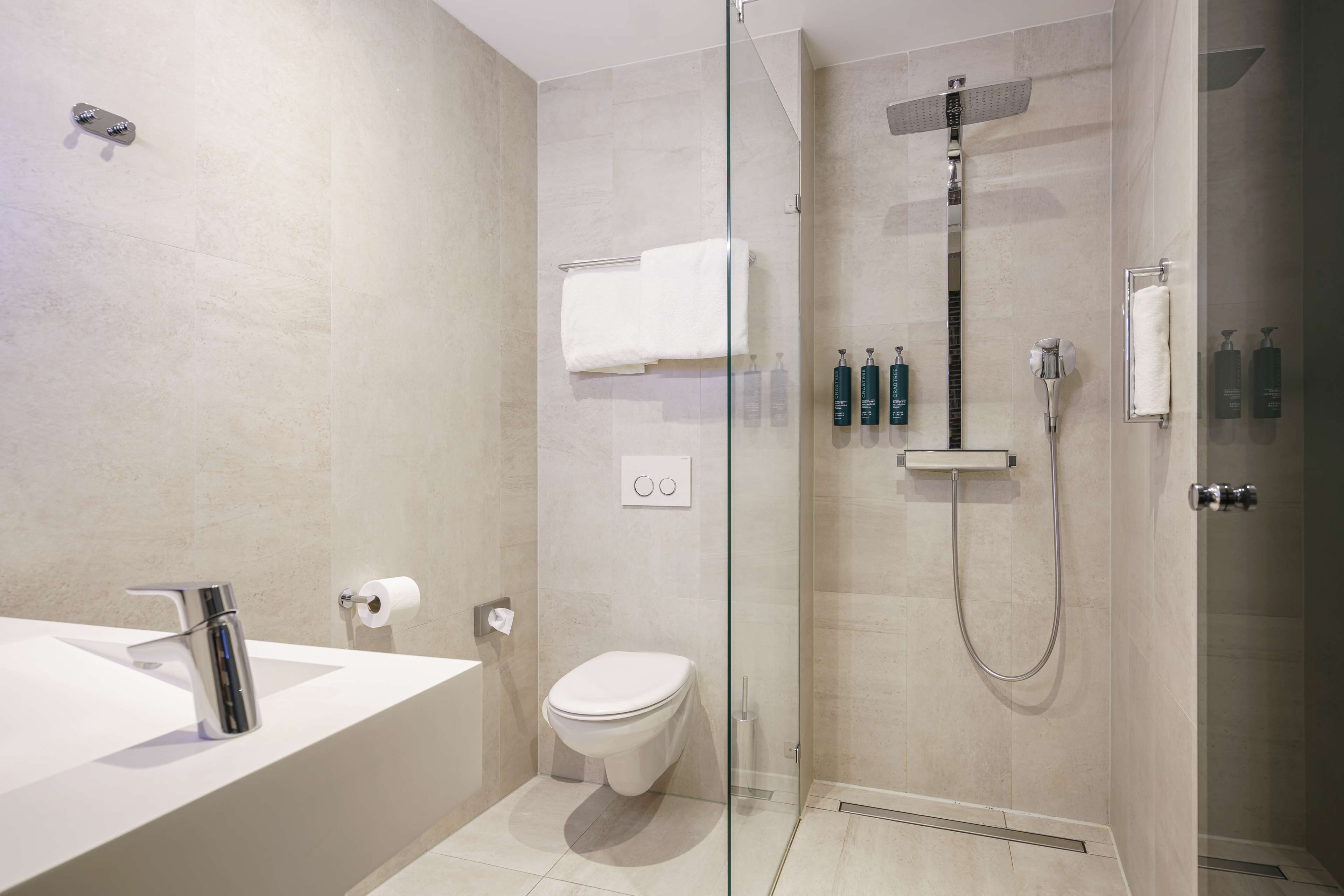 Un baño moderno con ducha de vidrio, un lavabo blanco y un inodoro.