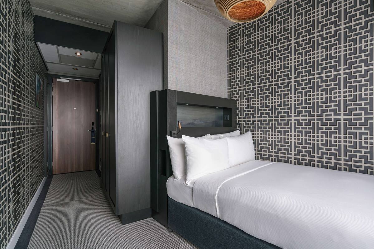 Une chambre d’hôtel moderne, équipée d’un lit, d’une télévision et d’un mur décoré de motifs.