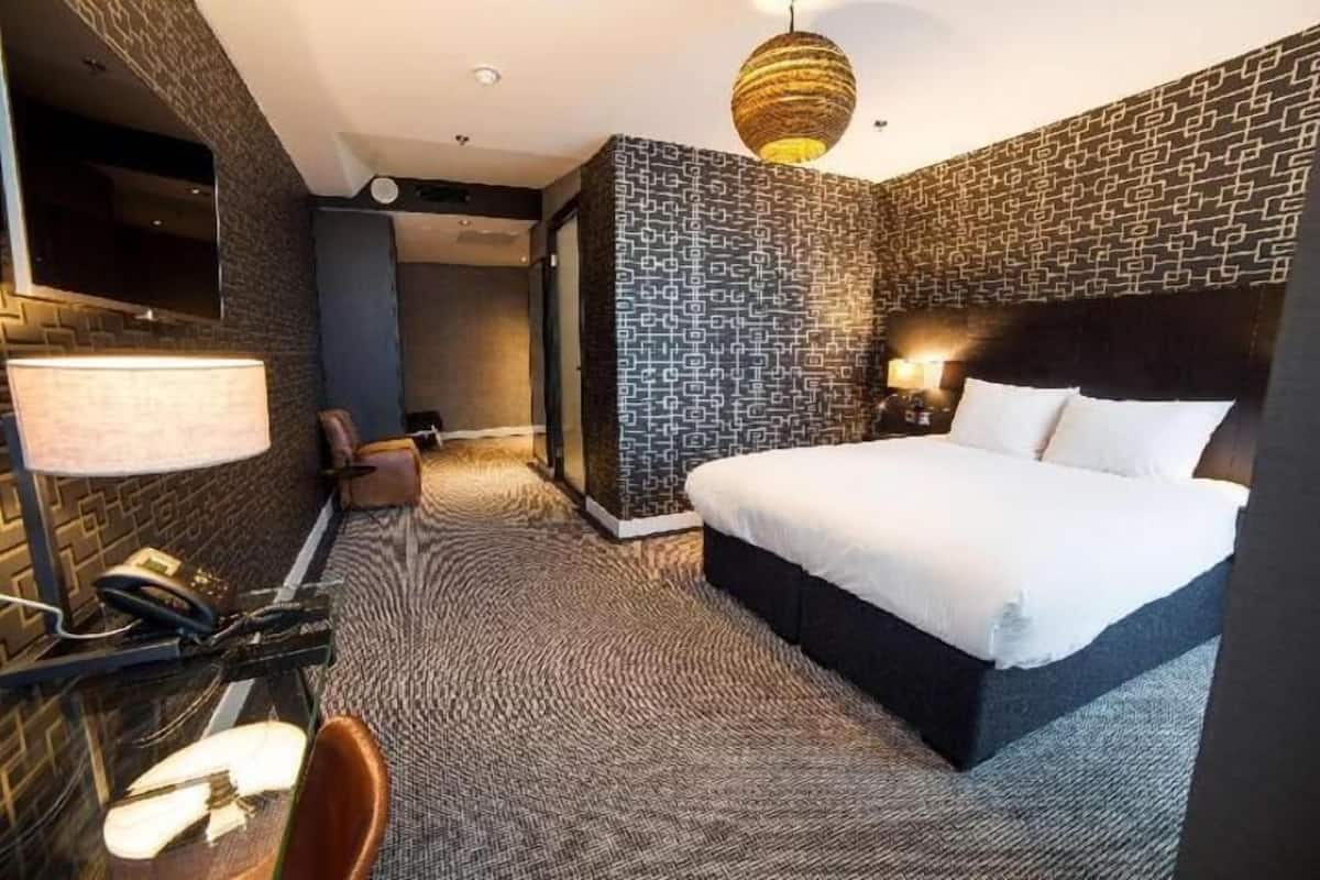 Une chambre d’hôtel avec un grand lit, un bureau avec une lampe, une chaise et un mur décoré d’un motif.